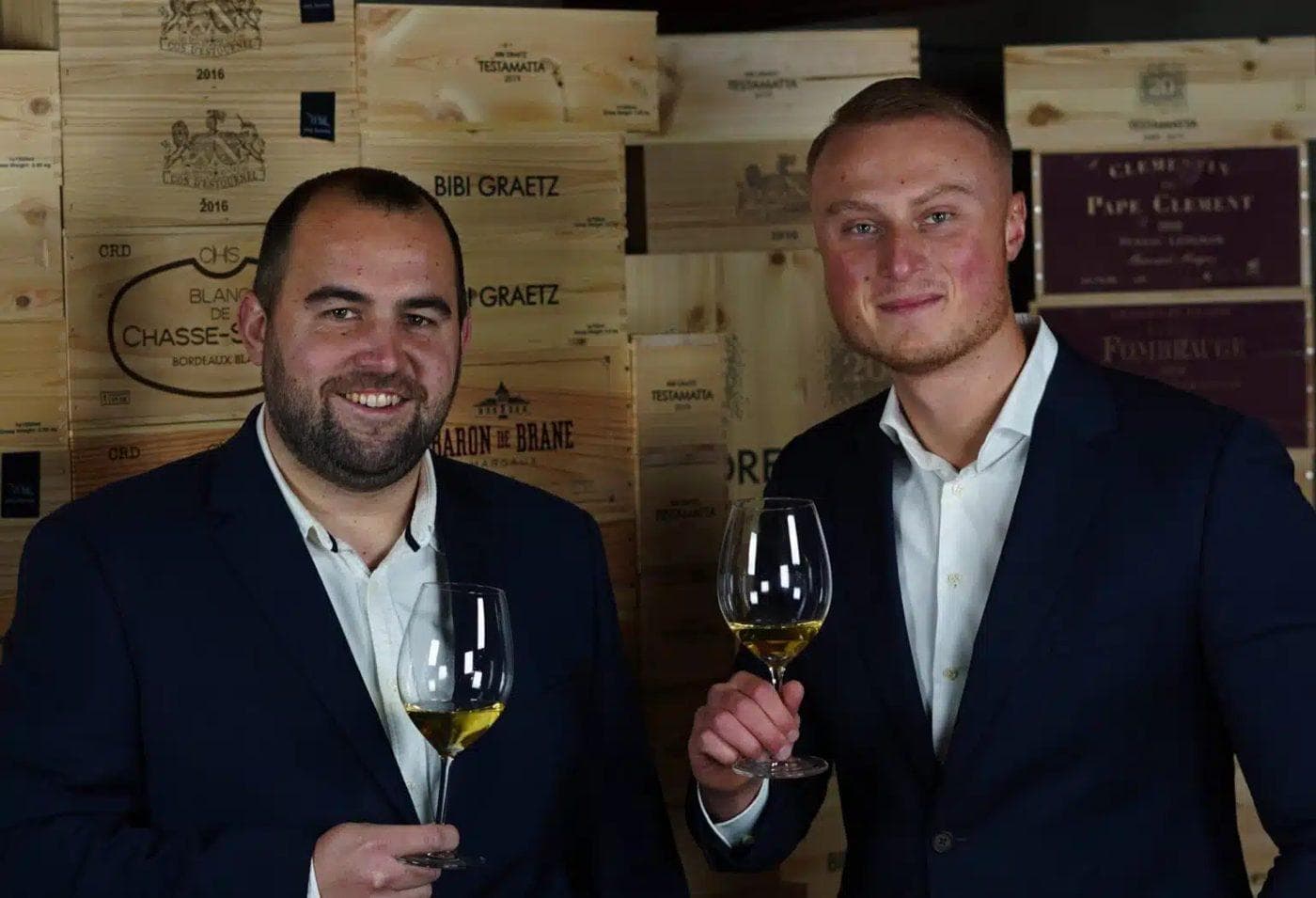 Jeffrey ten Oever en Bas Spée van Qualivin met een glas witte wijn voor een wand van wijnkisten