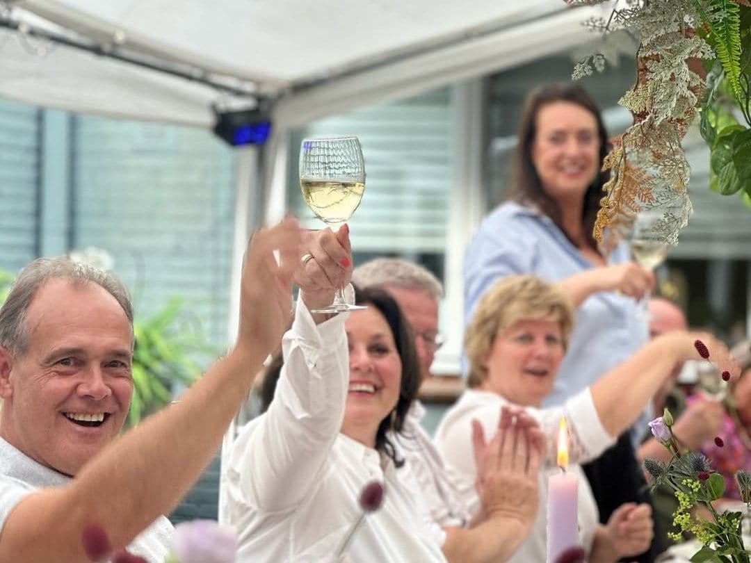 Gasten proosten lachend met een glas wijn aan tafel
